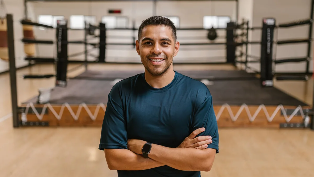 A fitness coach standing near a boxing ring, arms crossed, ready for questions about GoHighLevel for gyms