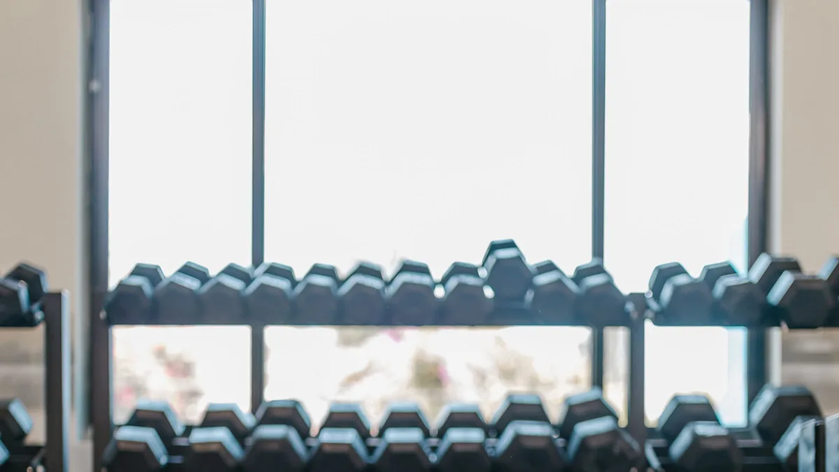 A dumbbell rack backlit by a bright window in an empty studio, representing the records behind GoHighLevel for gyms