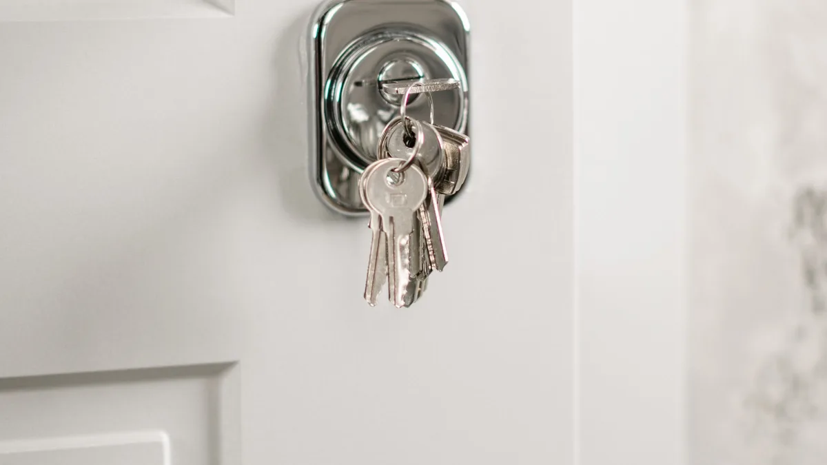 Plain keys hanging from a lock on a white door, representing who holds access in GoHighLevel for gyms