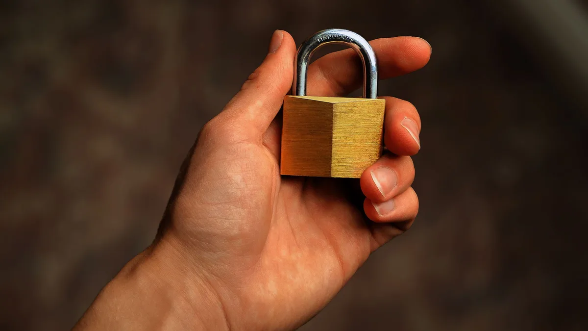 A hand holding a closed brass padlock, representing who controls billing data in GoHighLevel for gyms