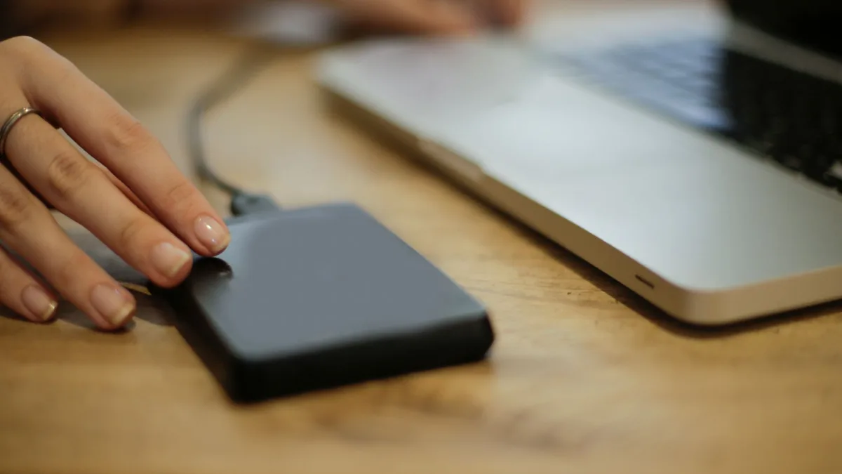 A hand connecting an external hard drive to a laptop to back up files before a sub-account transfer