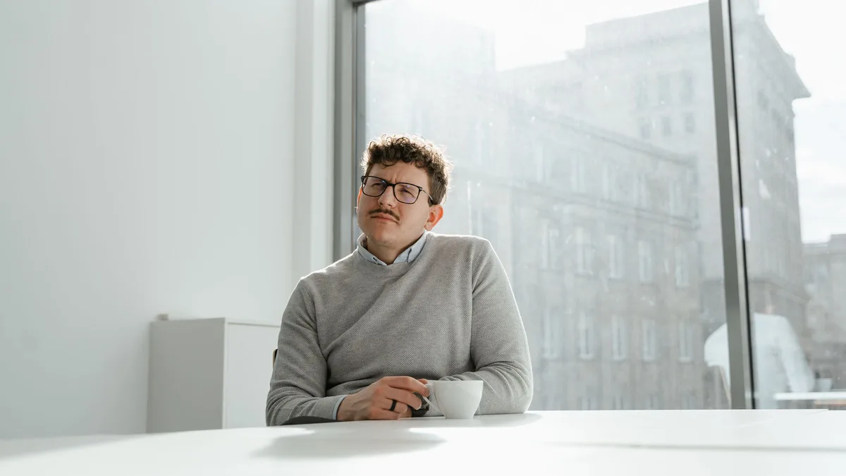 A business owner sitting by a window with coffee, thinking through sub-account transfer questions