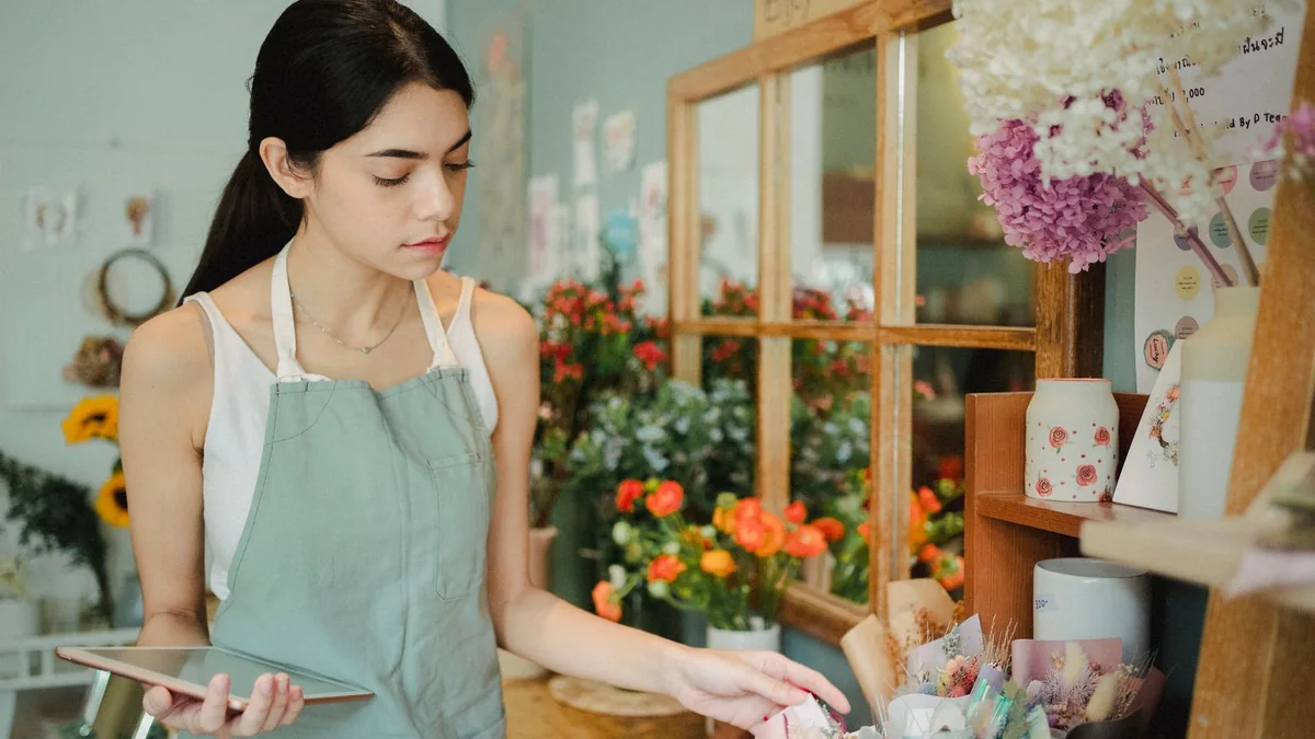 A florist checks a tablet beside her flower displays, from our GHL contact first name guide
