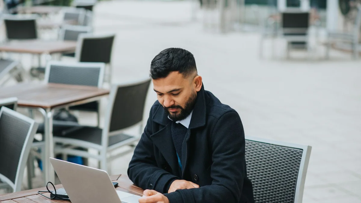 A business owner works on his laptop at an outdoor cafe, from our GHL maintenance retainer guide