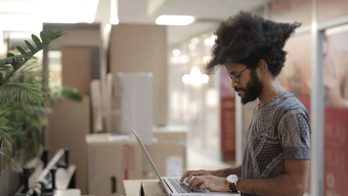 A shop owner works on his laptop among shipping boxes, from our GoHighLevel billing guide