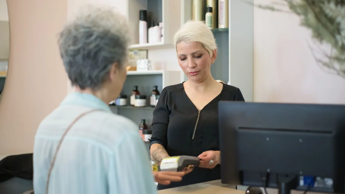 A salon owner takes a payment at the reception desk, from our GoHighLevel billing guide