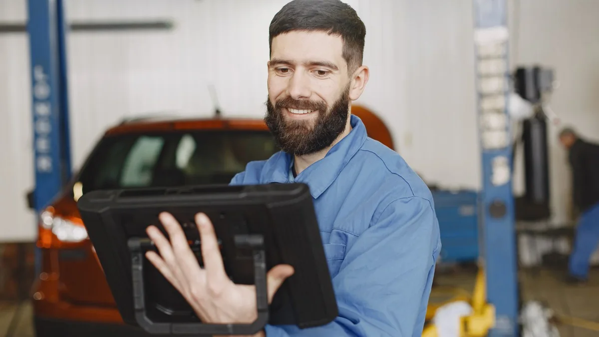 A mechanic smiles at a tablet in his garage, from our GoHighLevel reporting guide