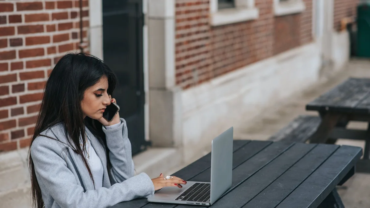 A woman follows up by phone with her laptop open at an outdoor table, from our GoHighLevel support guide