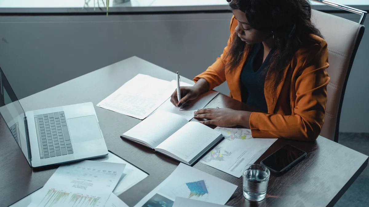 A business owner writes notes beside her laptop, from our GoHighLevel support guide