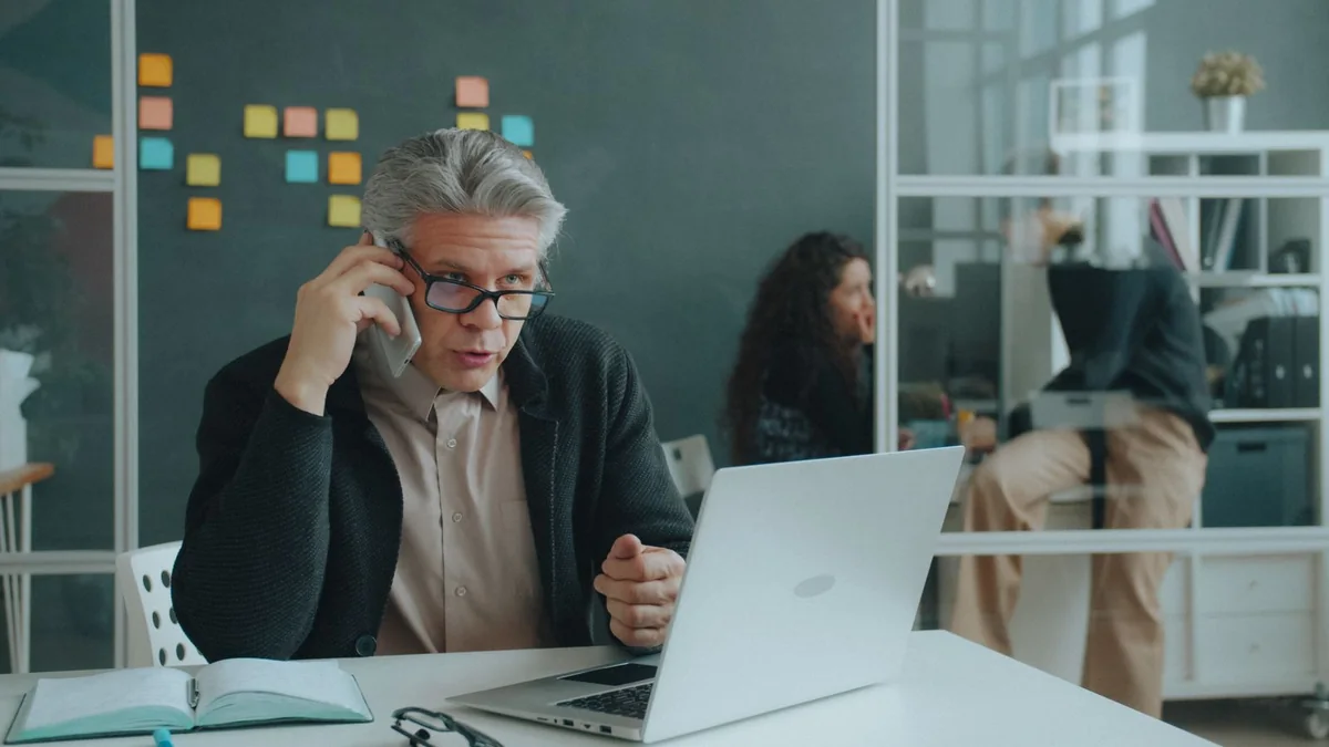 An older business owner takes a call at his laptop, from our GoHighLevel support guide