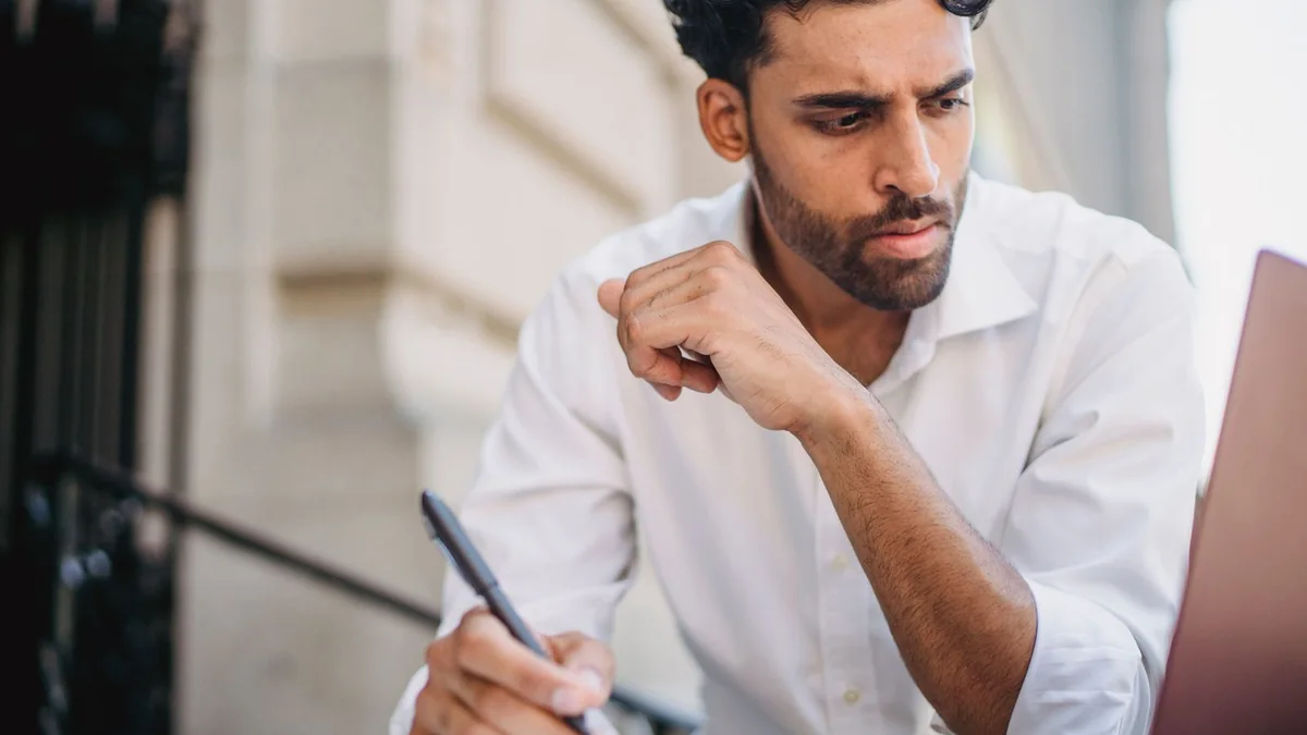 A business owner writes notes beside his laptop, from our HighLevel AI pricing guide