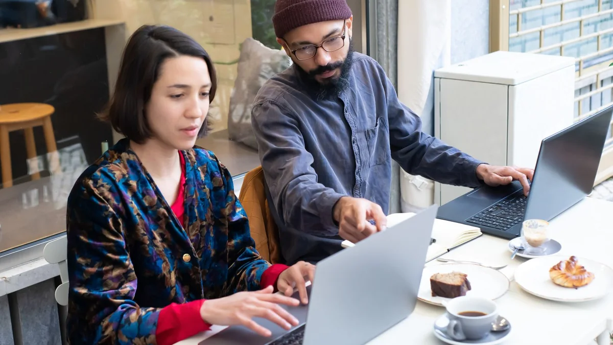 Two business partners compare laptops at a cafe table, from our import contacts guide